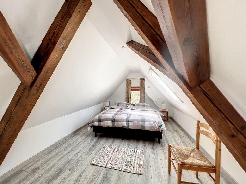 Chambre mansardée avec poutres apparentes, grand lit et parquet clair